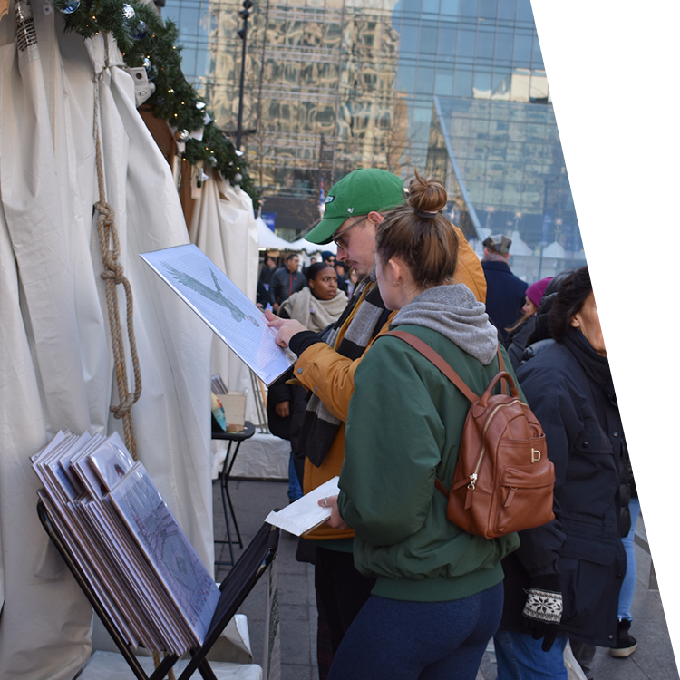 Woman and man at downtown Philadelphia outdoor holiday gift market hold and consider unframed Art of Words print.